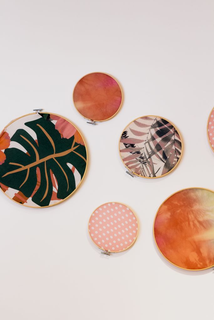 A vibrant display of circular embroidery hoops with abstract and botanical designs on a white wall.